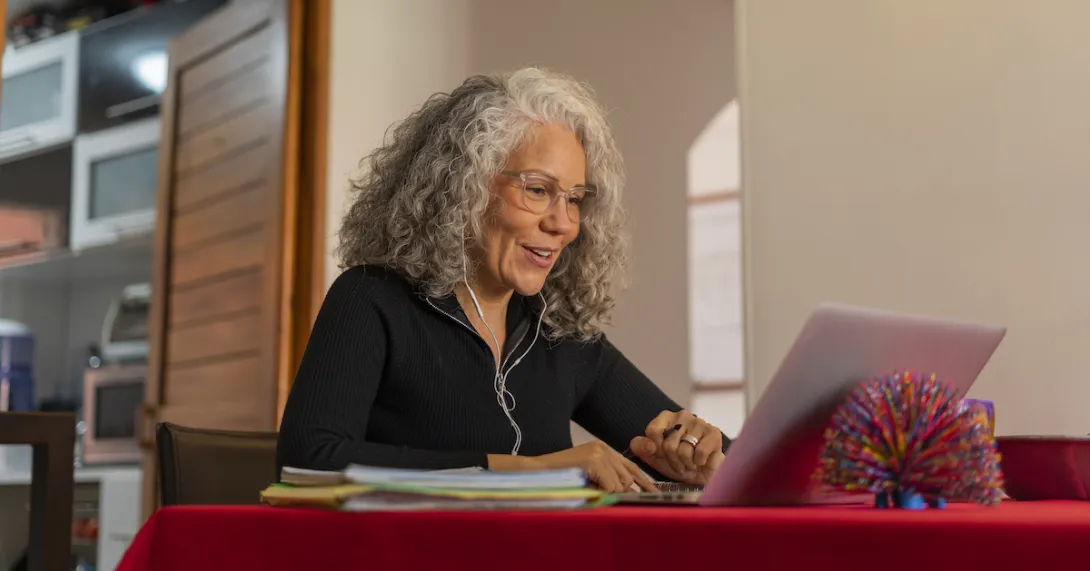 Person sitting at a dining room table looking at a computer Person sitting at a dining room table looking at a computer