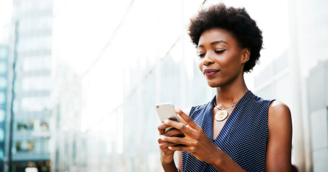 
  Person standing beside a building in a city looking at their phone
