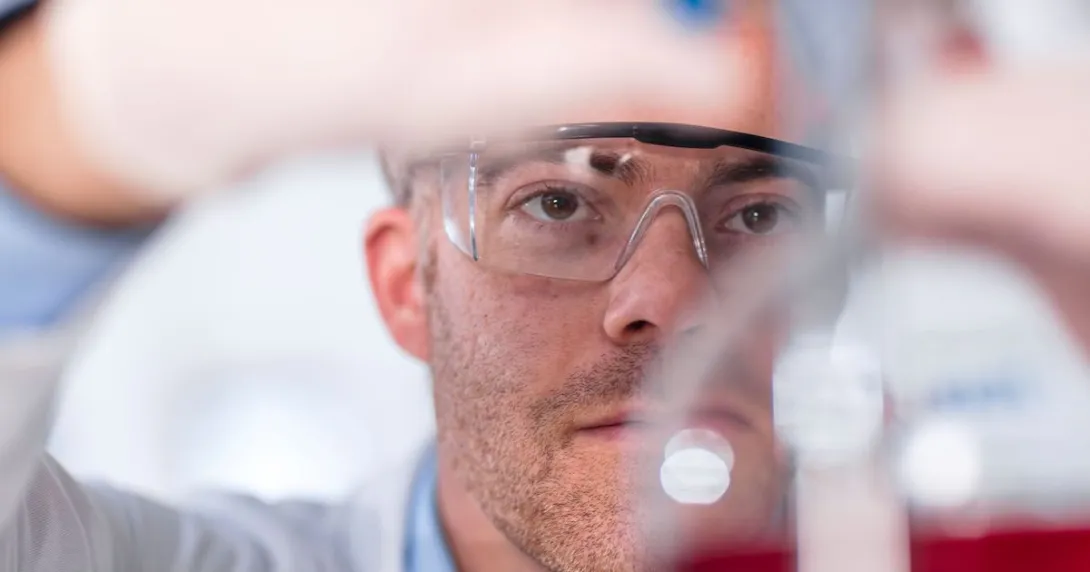 Scientist in a lab wearing safety goggles while putting something in a beaker