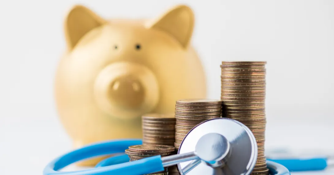 A piggy bank next to a pile of a coins and a stethoscope