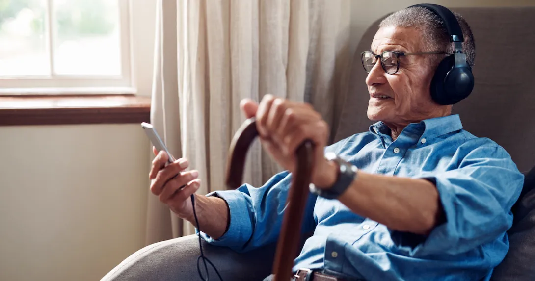 An older man wearing headphones and holding a smartphone